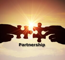 Partnership - two hands in silhouette, against a bright sun and orange sky, coming in, one from each side, each holding a jigsaw piece. Underneath is the word "Partnership".