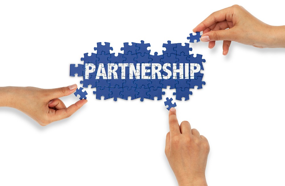 The Word Partnership being made up of jigsaw pieces, with three hands working on it.